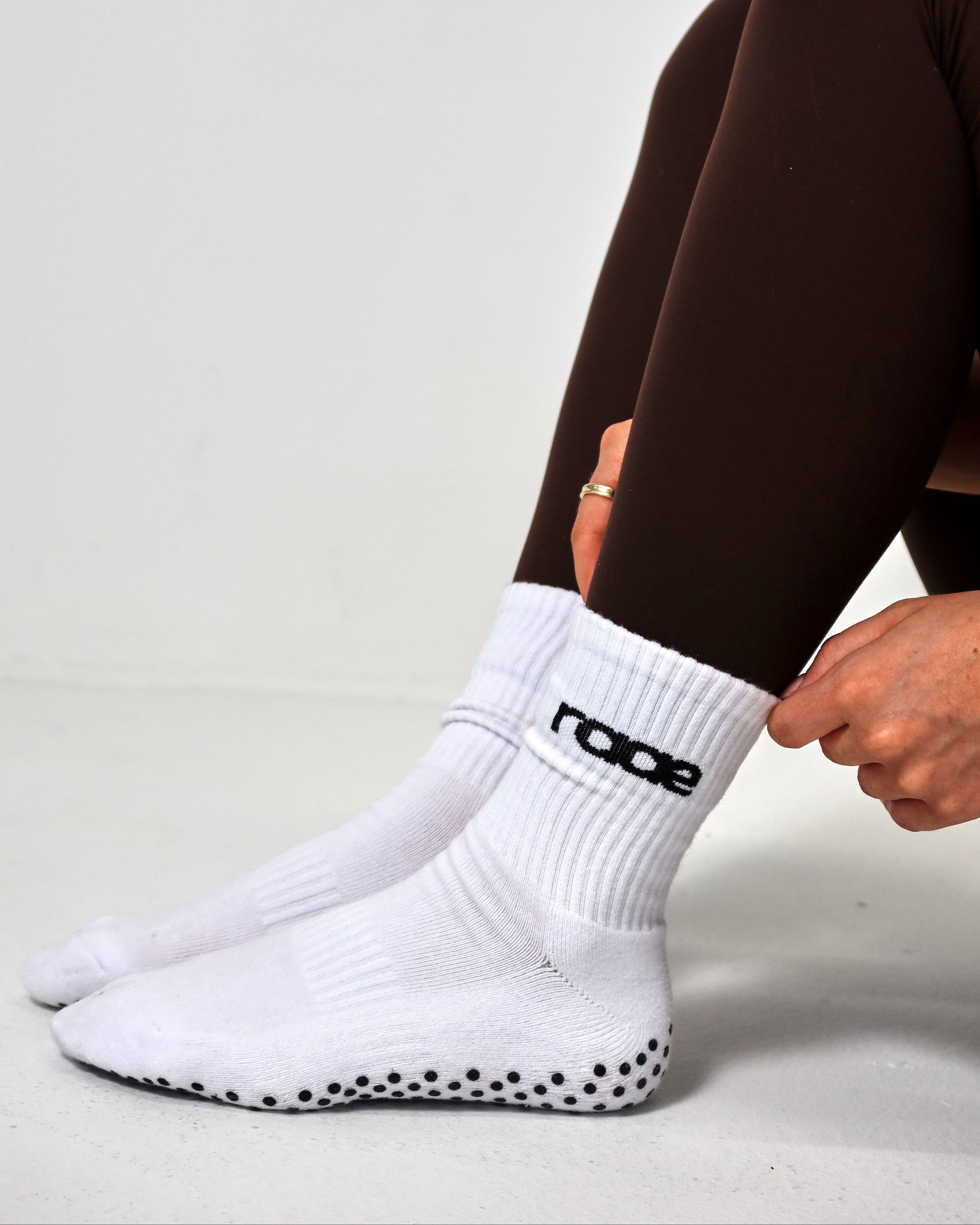 Person wearing white socks with black sole and 'raae' branding, sitting on a light gray background.
