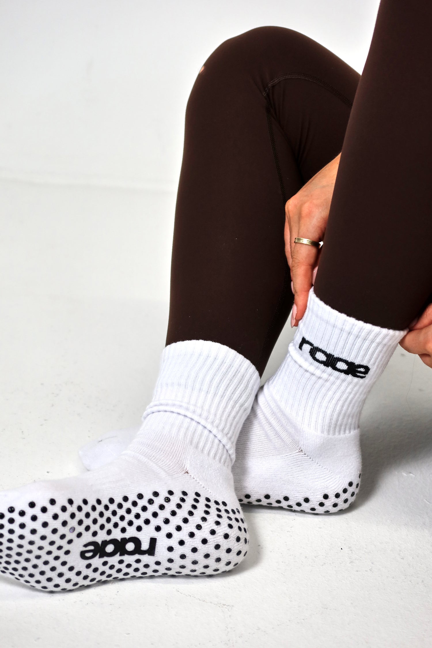 White socks with black grip dots and 'raize' branding worn by a person in brown leggings on a white background. activewear raae uk