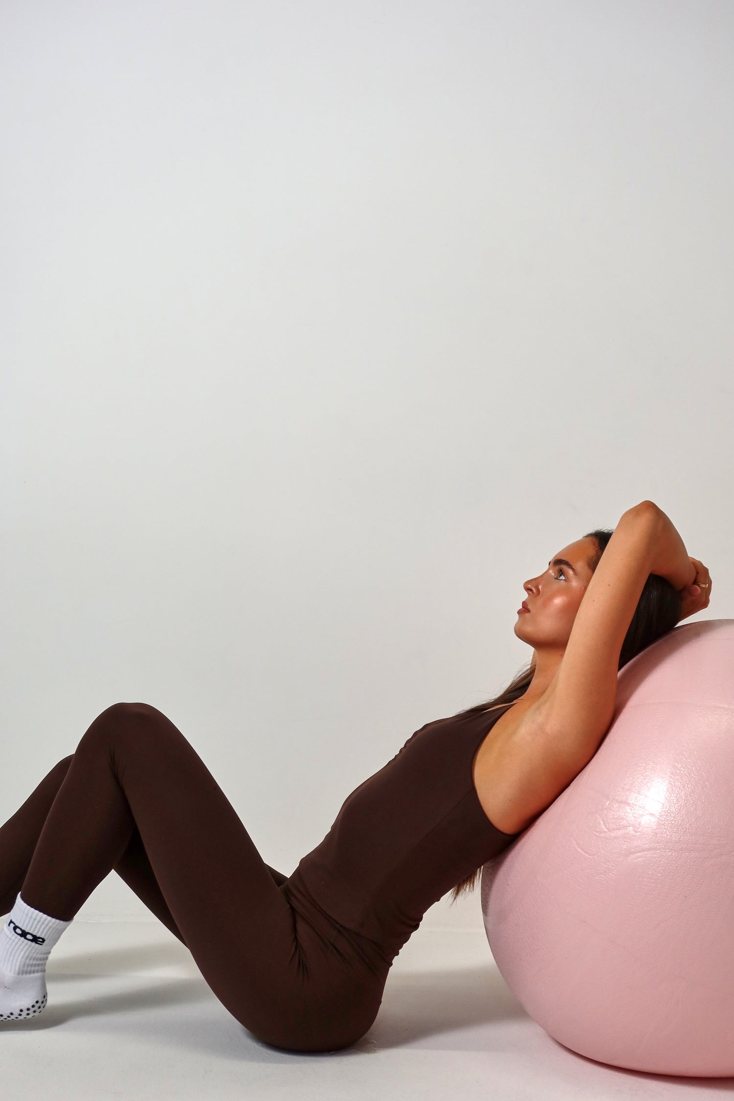 Woman exercising on a pink stability ball against a plain background activewear raae uk