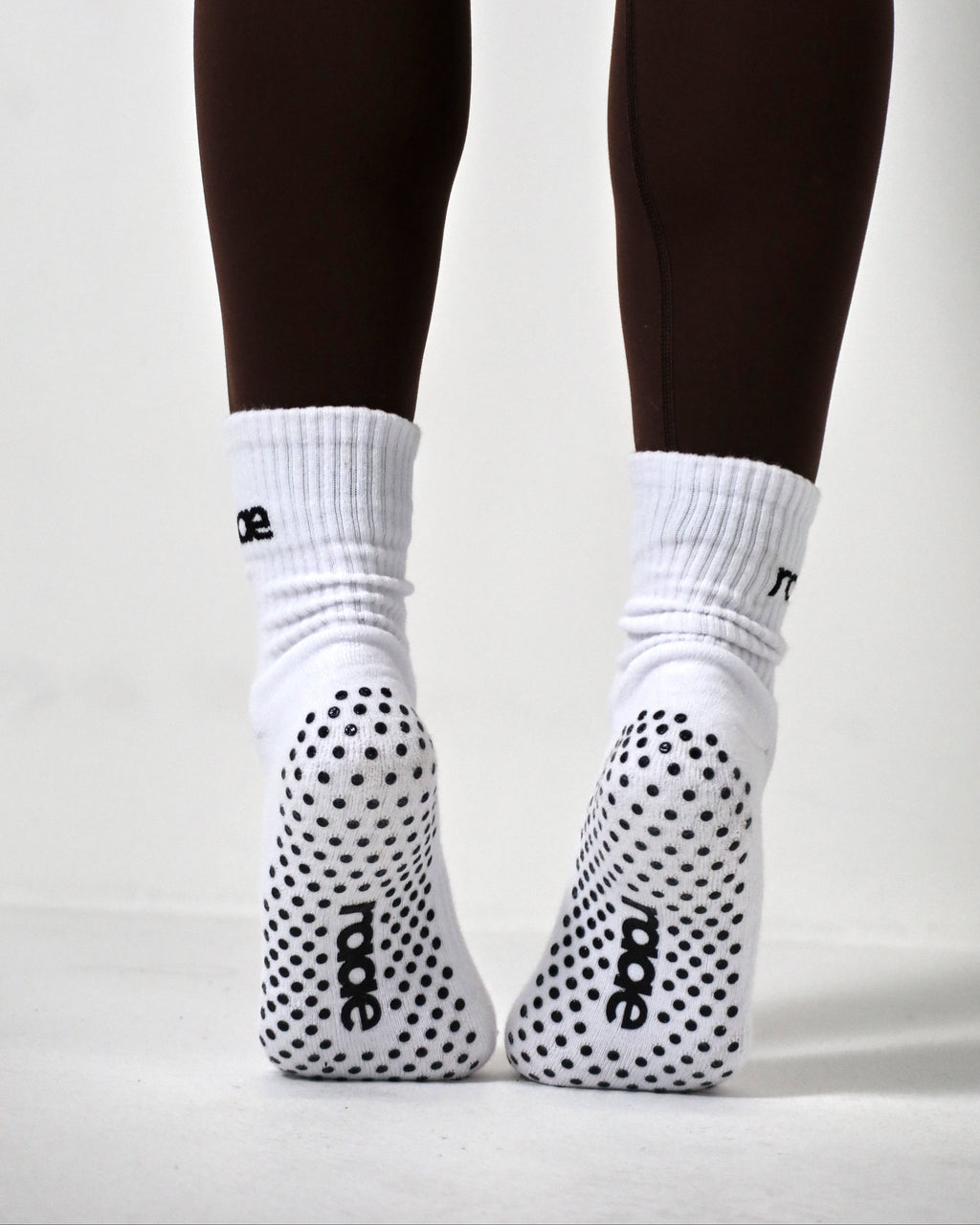 White socks with black polka dots and brand logo worn with dark leggings on a light gray background activewear raae uk